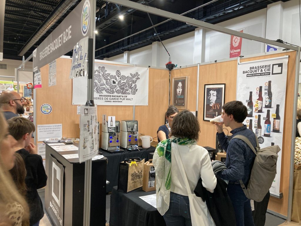 Le stand de la Brasserie Bacquet avec des comptoirs noirs sur les pourtours et une banderole au fond présentant leurs bières.