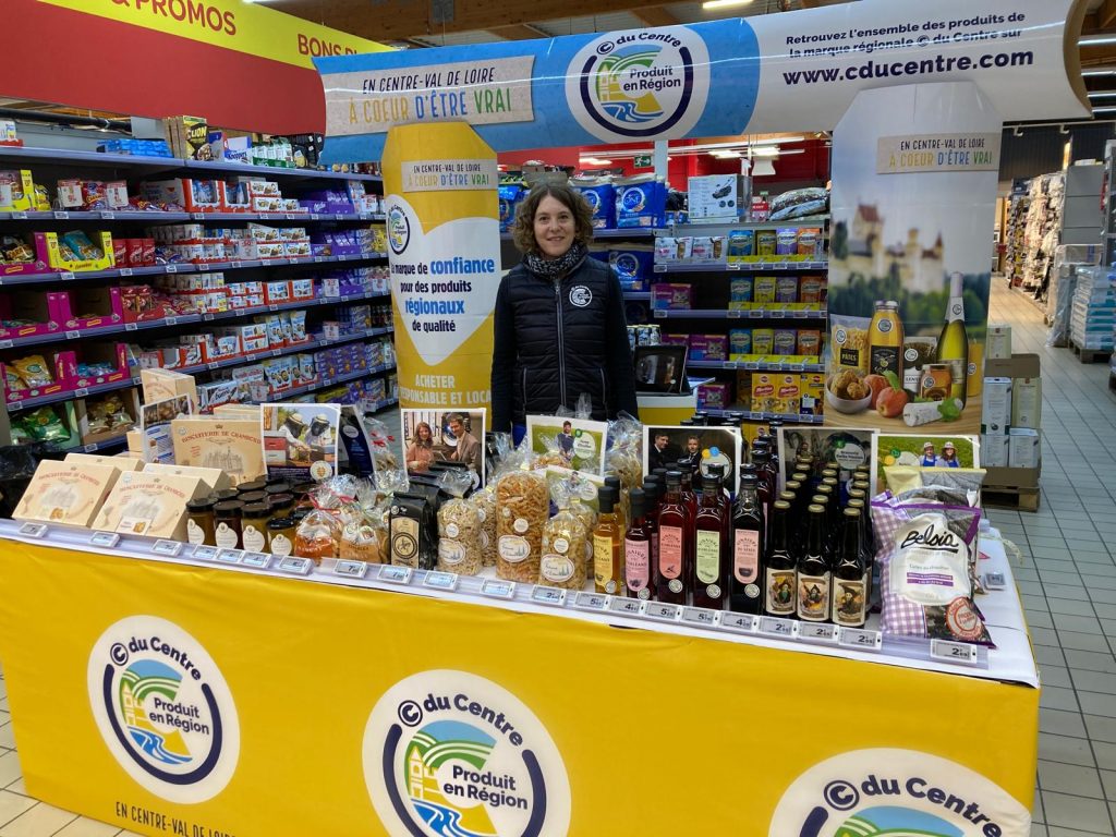 Stand promotionnel de la marque © du centre dans un supermarché présentant une sélection de produits régionaux tels que des bouteilles de bière ou de vinaigre, des pâtes ensachées et des miels et biscuits.