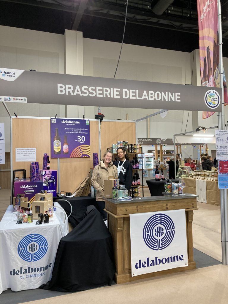 Le stand Brasserie Delabonne avec un comptoir en bois sur le devant et des bières delabonne.