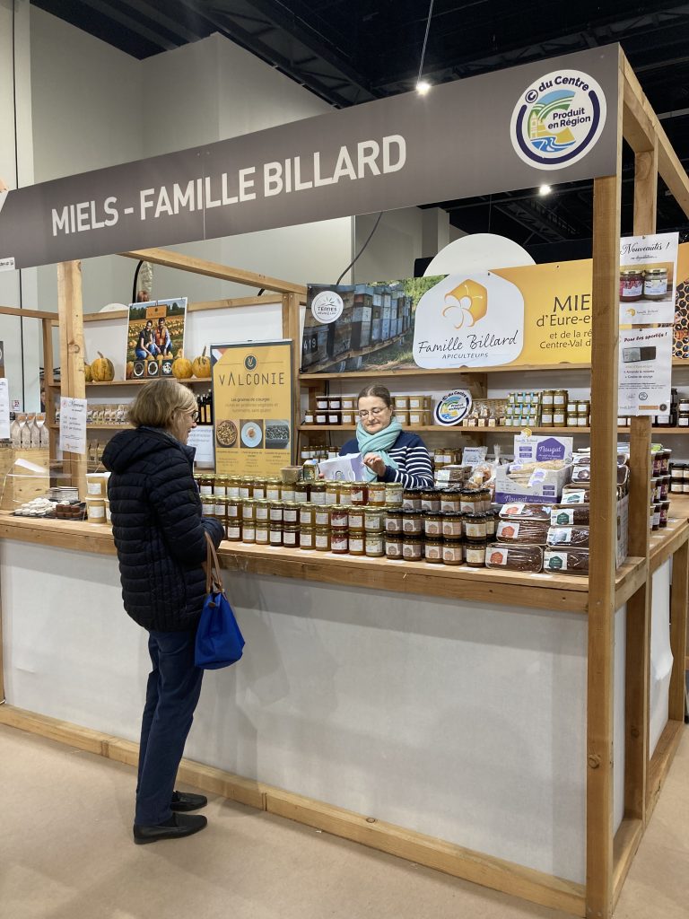 Le stand de Miels Billard avec des étagères bois sur lesquelles sont disposées des pots de miels. Au premier plan, il y a un comptoir avec 3 rangées de pots de miel.