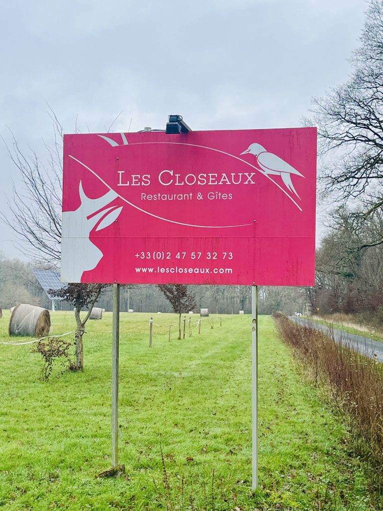 La pancarte "Les Closeaux, restaurant et gîtes" plantée dans un parc verdoyant le long d'une route.