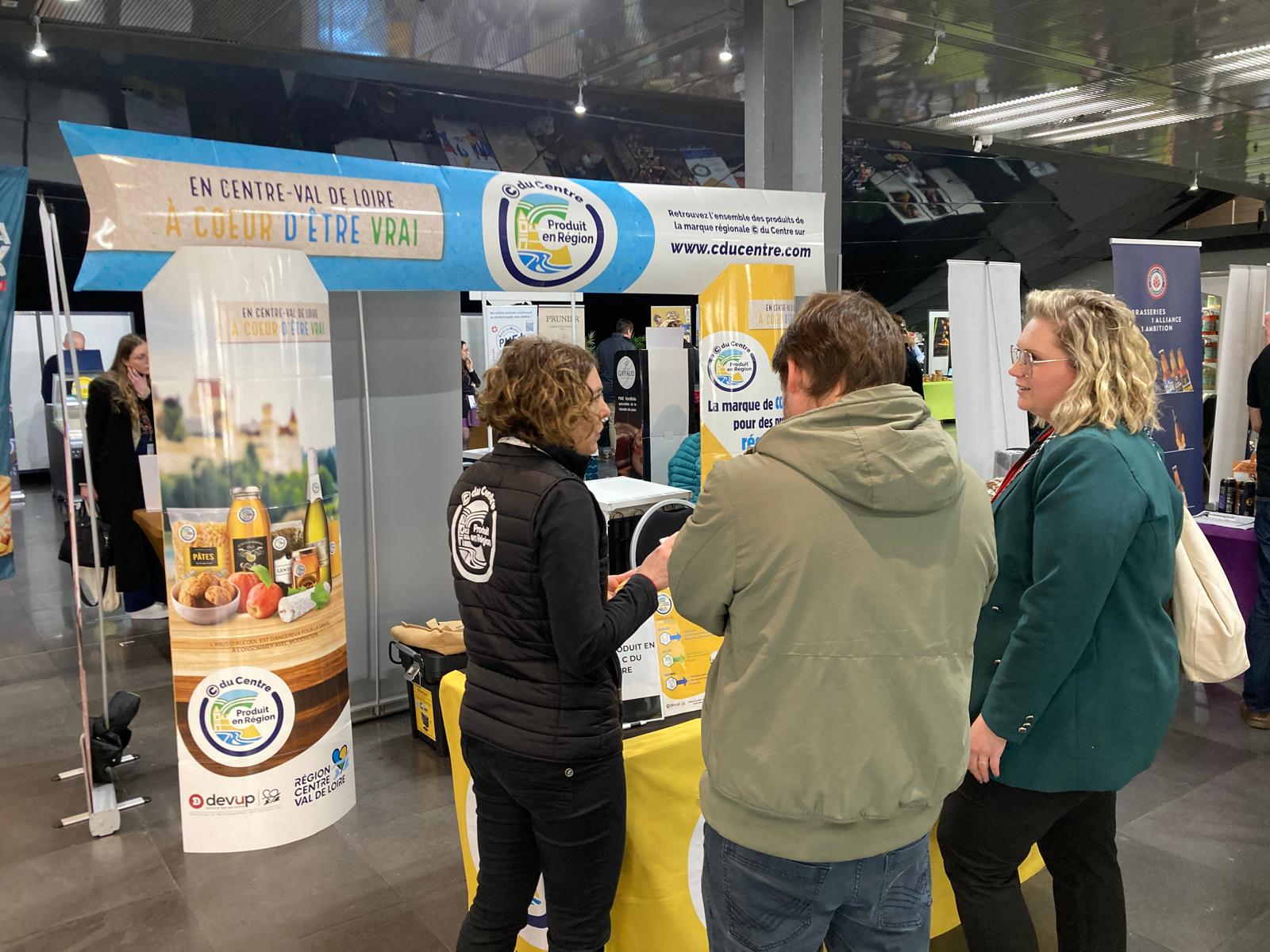 Stand de la marque régionale © du Centre au salon professionnel Auchan Grand Ouest, avec l’équipe © du Centre en discussion avec des représentants de magasins, présentant les services et produits locaux sous la bannière "Produit en Région © du Centre"..